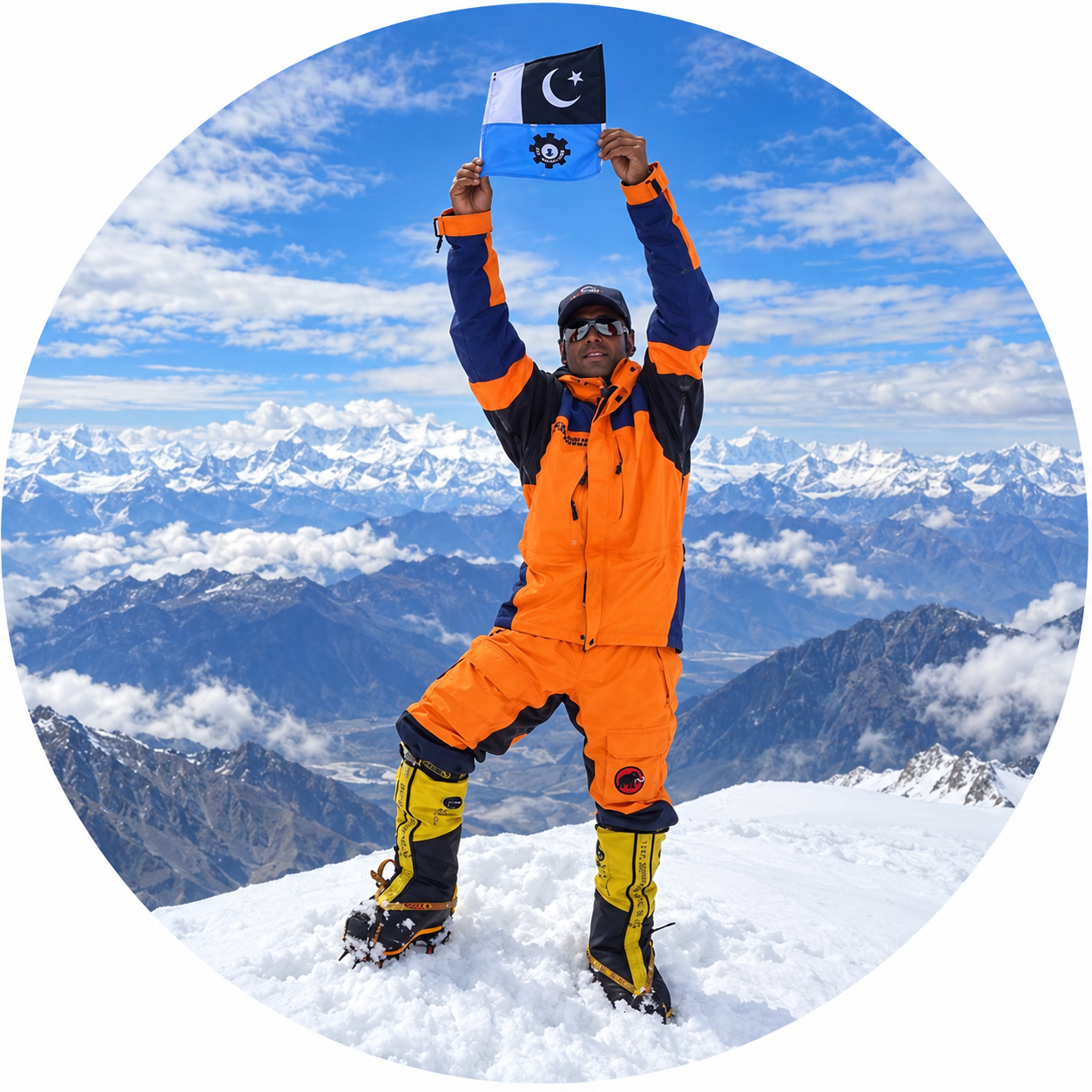 A climber in bright orange gear proudly holds a flag atop a snowy mountain peak with stunning mountain views.
