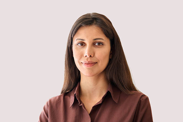 Confident woman with long dark hair wearing a brown shirt, smiling against a light background.